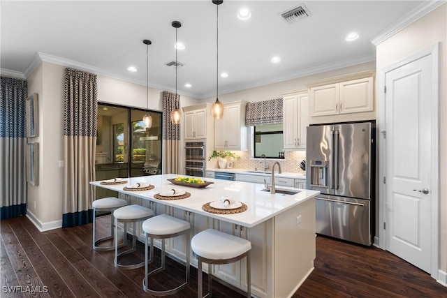 kitchen featuring a breakfast bar, hanging light fixtures, stainless steel appliances, ornamental molding, and a center island with sink