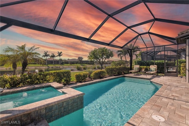 pool at dusk featuring an in ground hot tub, glass enclosure, and a patio