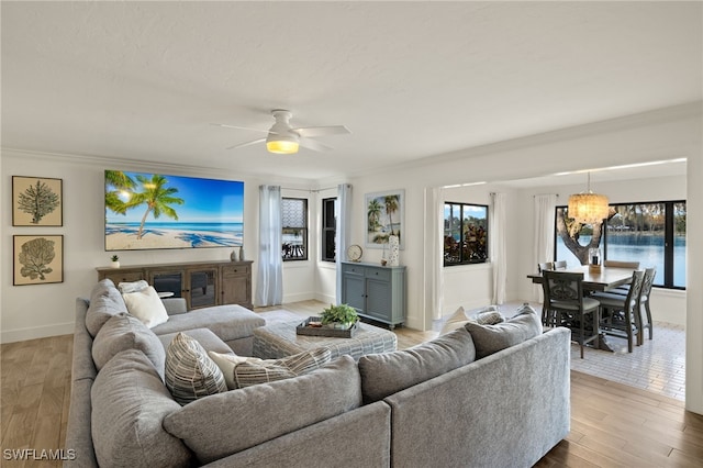 living room with ornamental molding, ceiling fan with notable chandelier, and light wood-type flooring