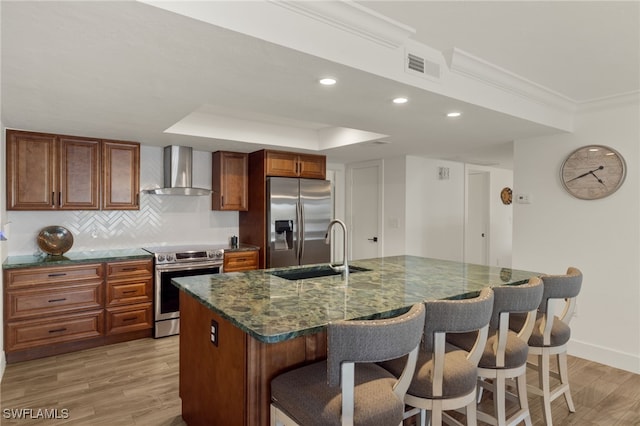 kitchen with sink, appliances with stainless steel finishes, backsplash, an island with sink, and wall chimney exhaust hood