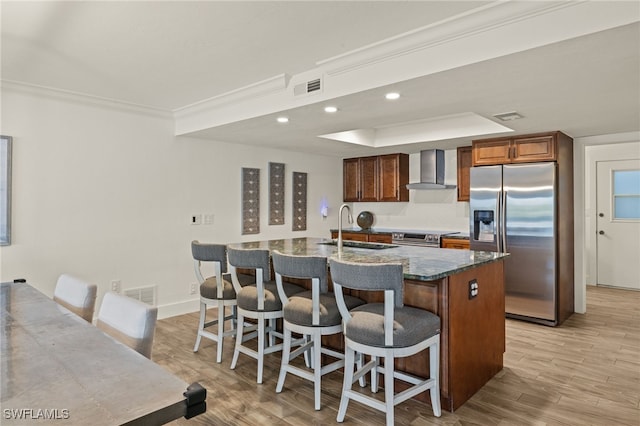 kitchen featuring appliances with stainless steel finishes, sink, wall chimney exhaust hood, a center island with sink, and light hardwood / wood-style flooring