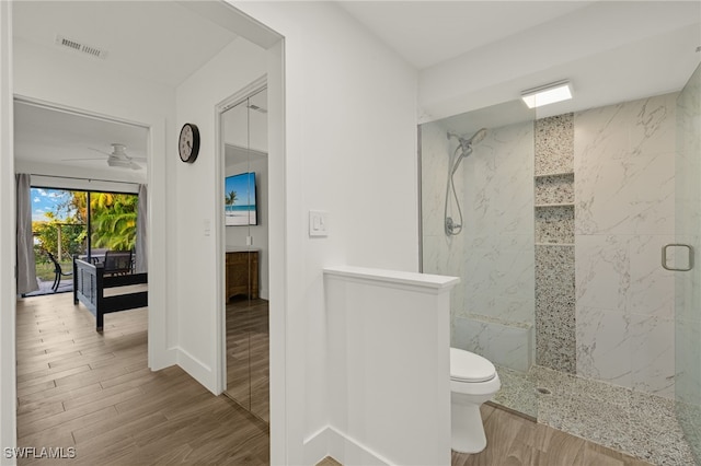 bathroom featuring ceiling fan, wood-type flooring, toilet, and a tile shower