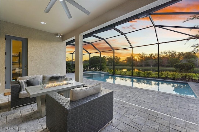 pool at dusk with an in ground hot tub, a lanai, a patio area, and an outdoor living space with a fire pit