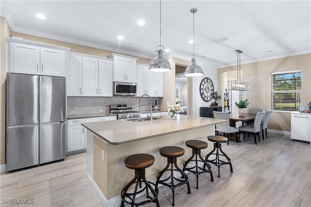 kitchen with a breakfast bar, white cabinetry, hanging light fixtures, stainless steel appliances, and a center island with sink