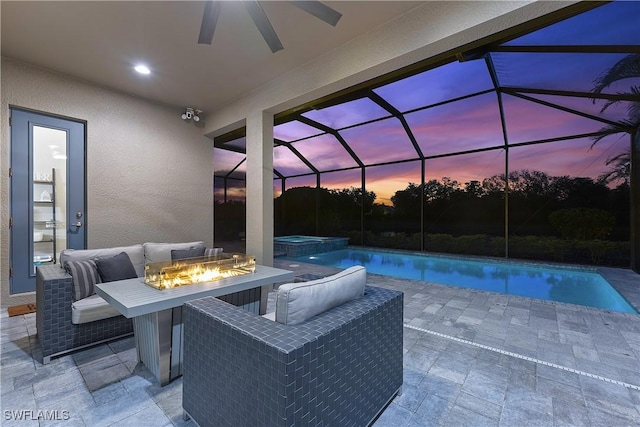 patio terrace at dusk featuring an outdoor fire pit, a pool with hot tub, and glass enclosure