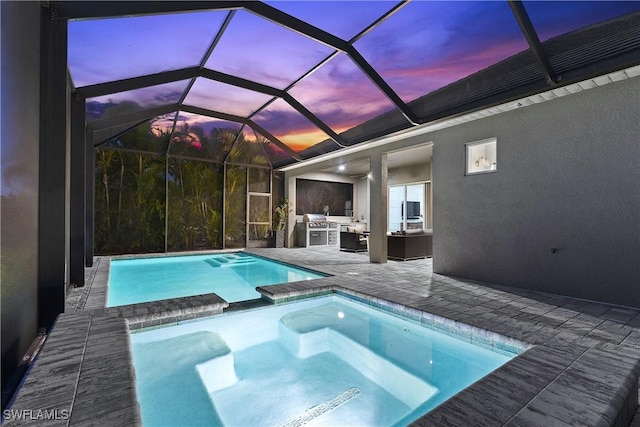 pool at dusk with outdoor lounge area, a patio, glass enclosure, an outdoor kitchen, and an in ground hot tub