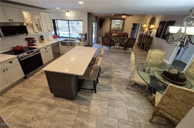 kitchen featuring white cabinetry, stainless steel appliances, a center island, tasteful backsplash, and a kitchen bar