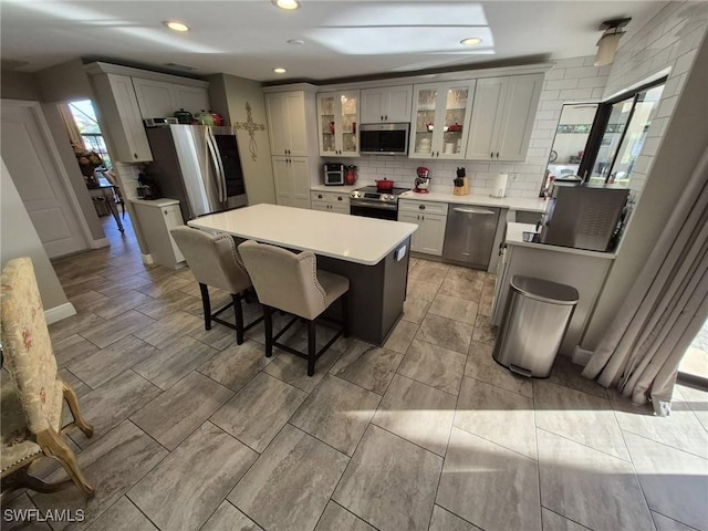 kitchen with appliances with stainless steel finishes, gray cabinets, a center island, and decorative backsplash