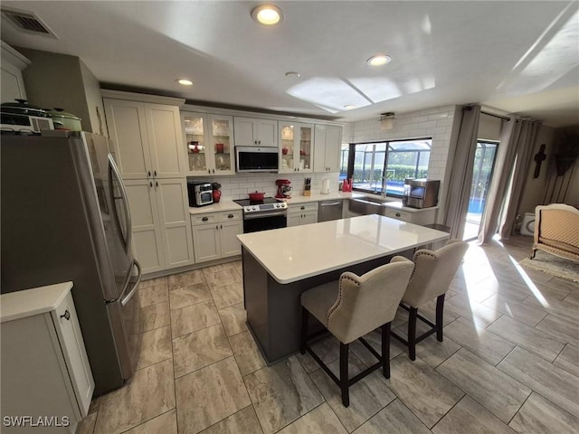 kitchen with sink, a breakfast bar area, backsplash, stainless steel appliances, and a kitchen island