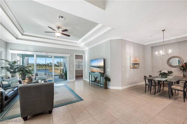 tiled living room featuring a raised ceiling, ornamental molding, and ceiling fan with notable chandelier