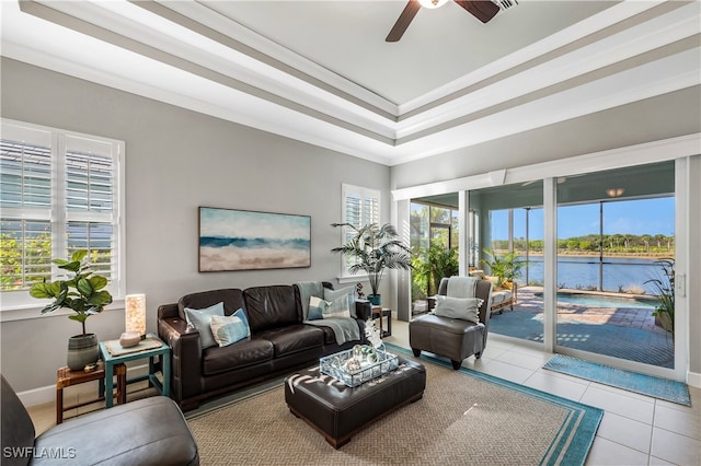 living room featuring ornamental molding, light tile patterned floors, ceiling fan, a raised ceiling, and a water view