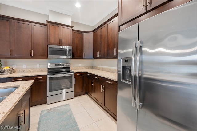 kitchen with stainless steel appliances, dark brown cabinetry, light stone counters, and light tile patterned floors