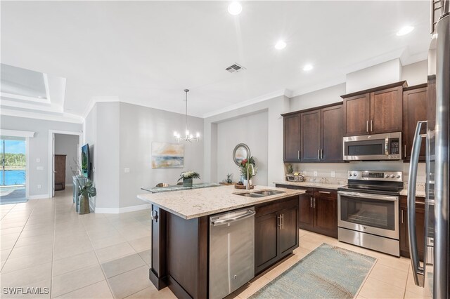 kitchen with decorative light fixtures, a kitchen island with sink, light stone counters, dark brown cabinetry, and stainless steel appliances