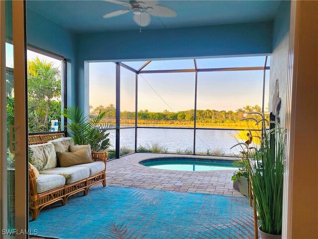 pool at dusk featuring a water view, ceiling fan, and a jacuzzi