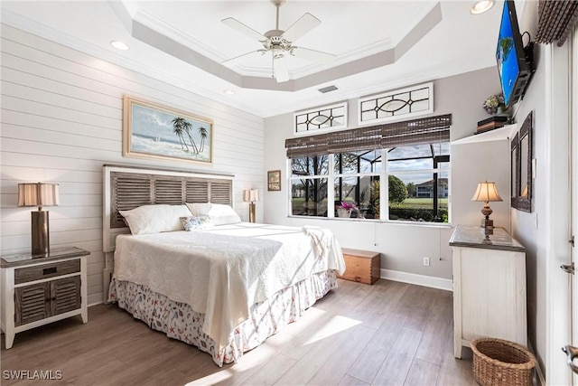 bedroom with hardwood / wood-style flooring, ceiling fan, crown molding, and a raised ceiling