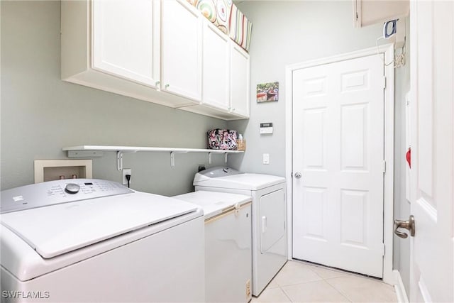 clothes washing area with cabinets, washing machine and dryer, and light tile patterned floors