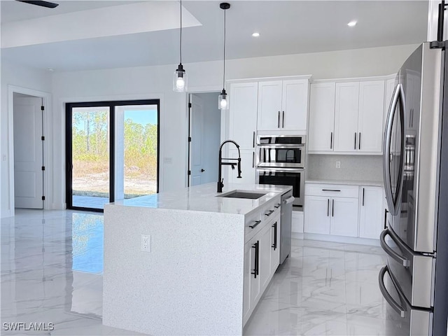 kitchen featuring light stone counters, appliances with stainless steel finishes, a center island with sink, and white cabinets