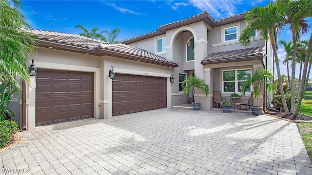 mediterranean / spanish-style house with a tile roof, decorative driveway, stucco siding, and an attached garage
