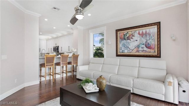 living area with a ceiling fan, visible vents, baseboards, dark wood-type flooring, and crown molding