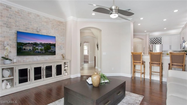 living area featuring a ceiling fan, dark wood-style floors, arched walkways, crown molding, and baseboards