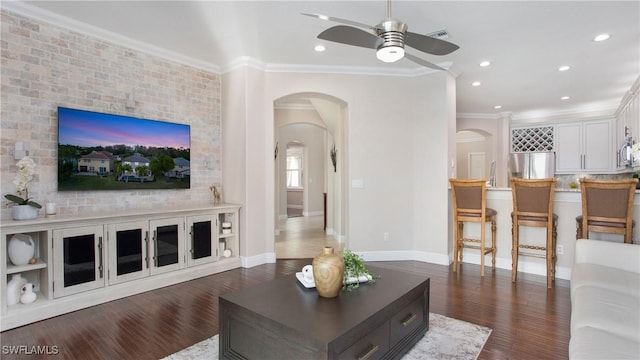 living room featuring dark wood finished floors, baseboards, arched walkways, ceiling fan, and ornamental molding