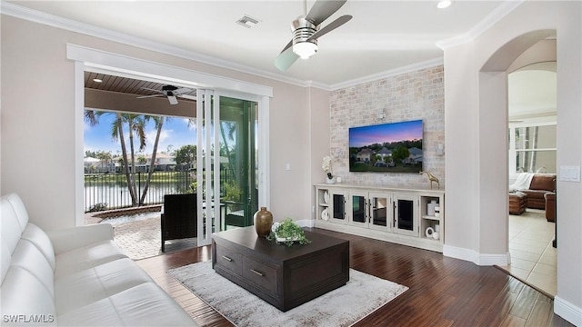 living room with a ceiling fan, wood finished floors, visible vents, arched walkways, and crown molding