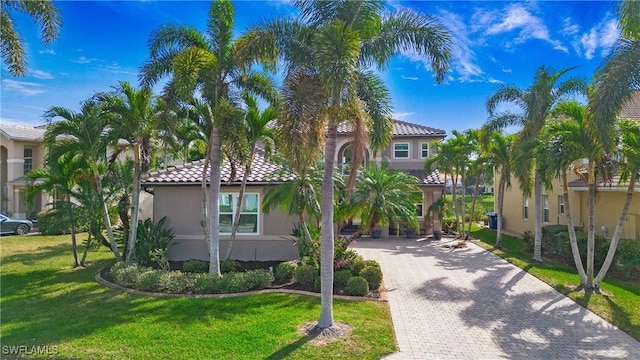 mediterranean / spanish home with stucco siding, a tile roof, decorative driveway, and a front lawn