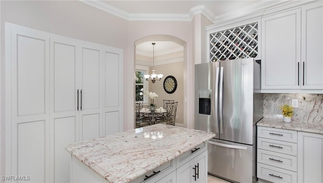 kitchen featuring light stone counters, arched walkways, stainless steel refrigerator with ice dispenser, crown molding, and tasteful backsplash