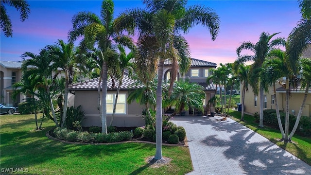 mediterranean / spanish house featuring decorative driveway, a tile roof, a front yard, and stucco siding