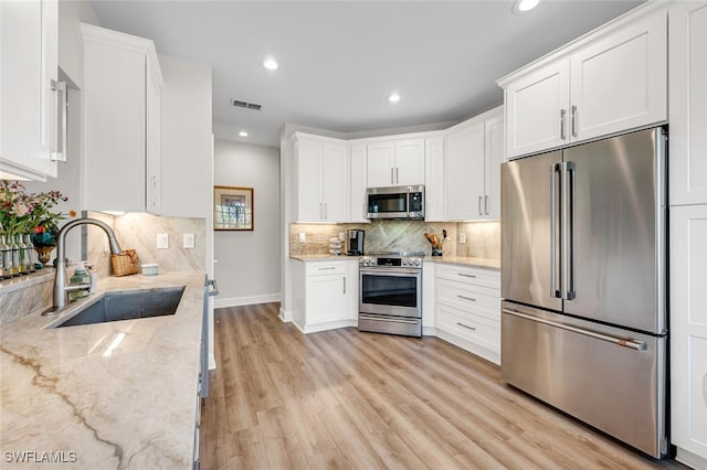 kitchen featuring white cabinetry, sink, stainless steel appliances, light stone countertops, and light hardwood / wood-style flooring