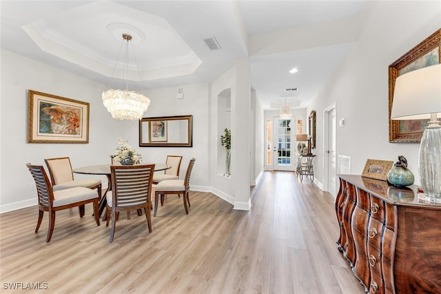 dining room featuring crown molding, a tray ceiling, a chandelier, and light wood-type flooring