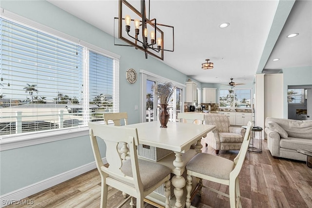 dining space with ceiling fan with notable chandelier and light hardwood / wood-style flooring