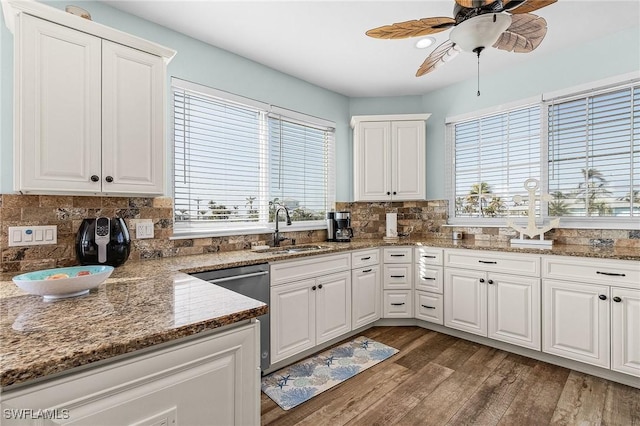 kitchen featuring sink, dark hardwood / wood-style floors, white cabinets, stainless steel dishwasher, and dark stone counters