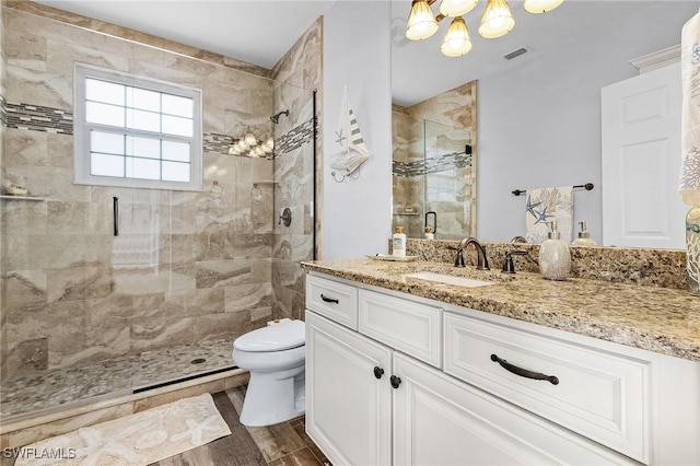 bathroom featuring a shower with door, an inviting chandelier, hardwood / wood-style floors, vanity, and toilet