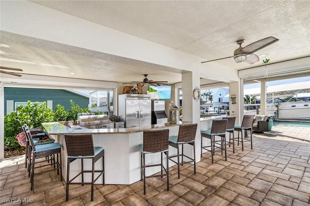 kitchen with a textured ceiling, a kitchen breakfast bar, built in fridge, and ceiling fan