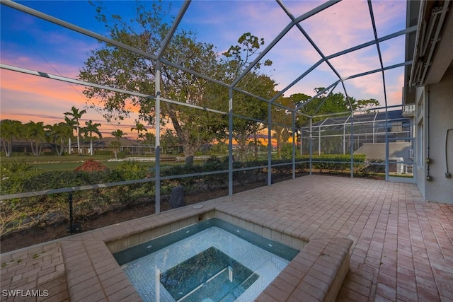 pool at dusk with an in ground hot tub, a lanai, and a patio area