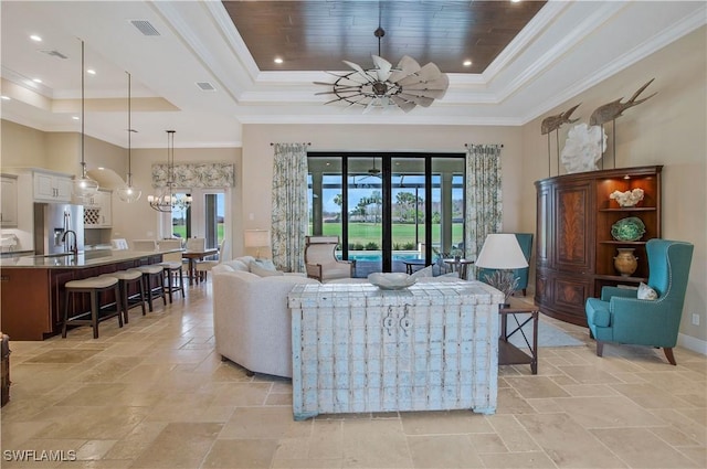 living room featuring ornamental molding, a healthy amount of sunlight, a raised ceiling, and ceiling fan with notable chandelier