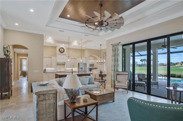 living room featuring a raised ceiling, crown molding, and ceiling fan with notable chandelier