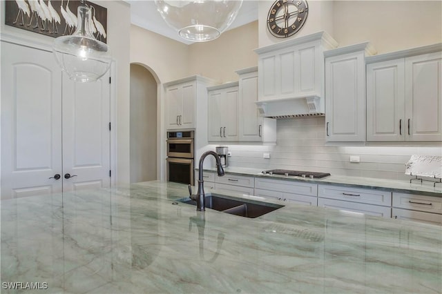 kitchen featuring hanging light fixtures, sink, white cabinets, and light stone counters