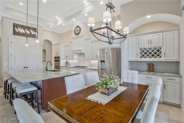 kitchen with appliances with stainless steel finishes, a kitchen island with sink, a tray ceiling, white cabinets, and decorative light fixtures