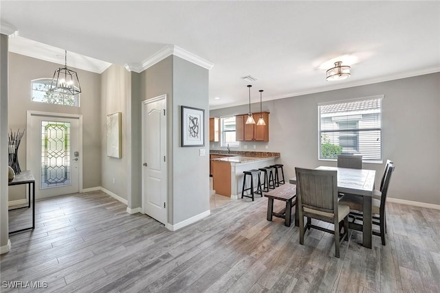 dining area featuring an inviting chandelier, sink, crown molding, and light hardwood / wood-style flooring