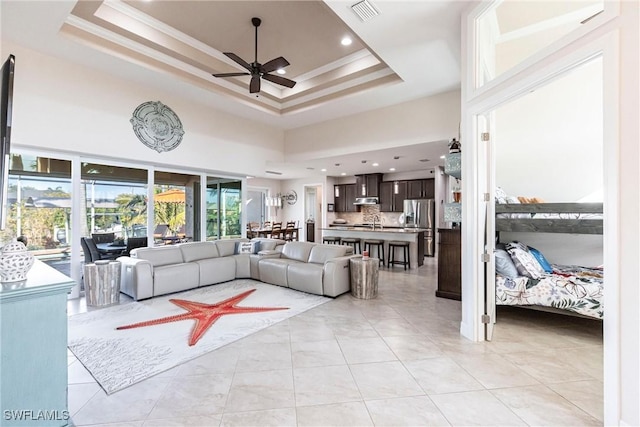 tiled living room with crown molding, ceiling fan, a raised ceiling, and a high ceiling