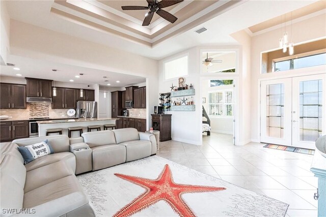 tiled living room with a towering ceiling, ornamental molding, a raised ceiling, an inviting chandelier, and french doors