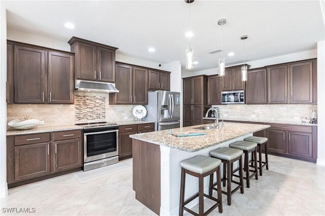 kitchen featuring appliances with stainless steel finishes, pendant lighting, sink, a kitchen island with sink, and light stone counters