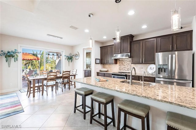 kitchen with sink, hanging light fixtures, appliances with stainless steel finishes, light stone countertops, and decorative backsplash