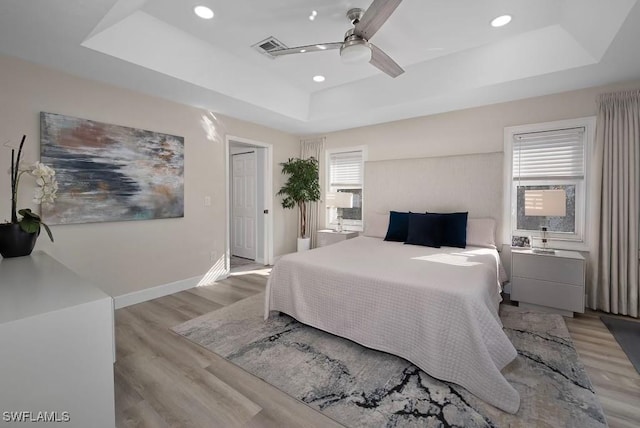 bedroom with ceiling fan, a tray ceiling, and light hardwood / wood-style floors