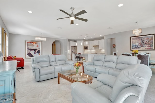 tiled living room with ceiling fan with notable chandelier