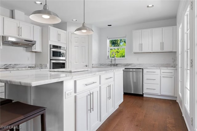 kitchen featuring white cabinetry, stainless steel appliances, dark hardwood / wood-style floors, a center island, and decorative light fixtures