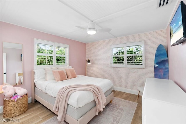 bedroom with light wood-style flooring, an accent wall, brick wall, visible vents, and baseboards