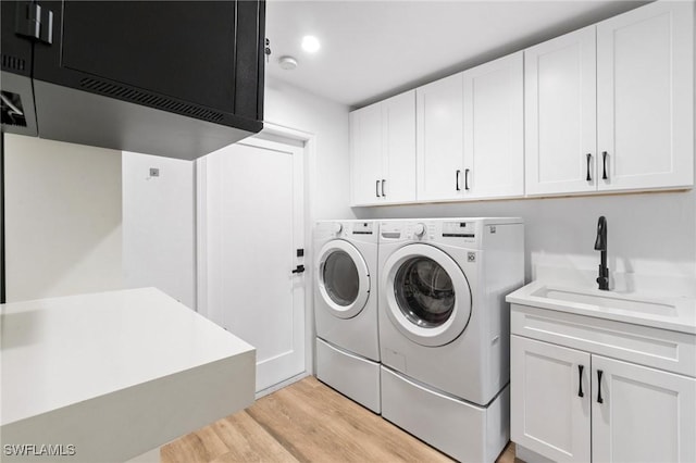 laundry area featuring light wood finished floors, cabinet space, washer and dryer, and a sink